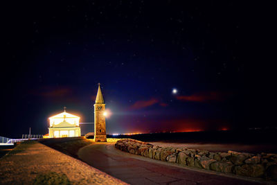 Illuminated castle by sea against sky at night