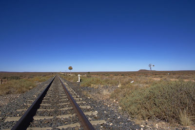 Railroad tracks on field against clear blue sky