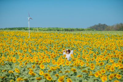 Woman standing amidst sunflowers against clear blue sky