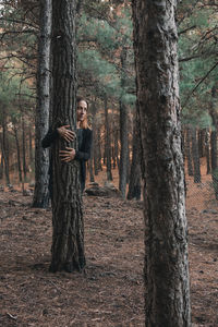 Portrait of man standing by tree trunk in forest