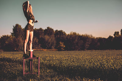 Young woman standing on equipment over field against clear sky during sunset