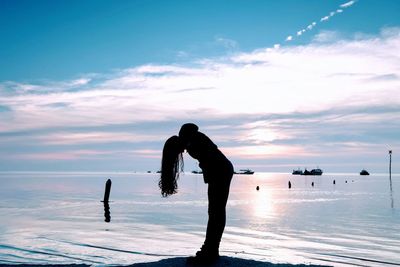 Silhouette of woman standing at beach against sky during sunset