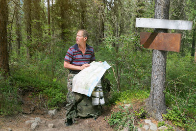 Man holding map over backpack against trees in forest