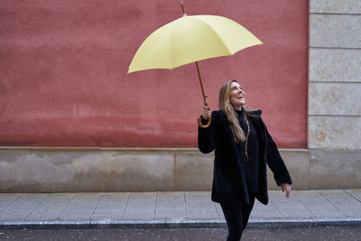 Pretty girl plays in the street with her yellow umbrella while laughing.