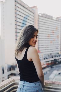 Rear view of young woman standing against buildings in city