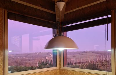 Illuminated lamp by buildings against sky seen through glass window