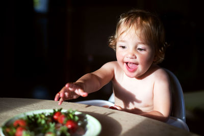 Cute baby girl reaching towards food in plate