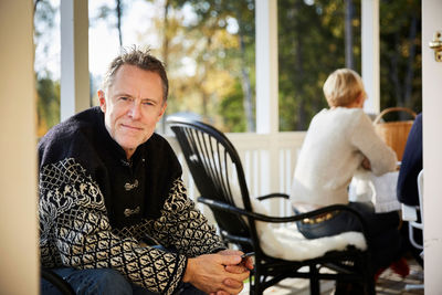 Portrait of smiling mature man sitting on porch with friend sitting in background