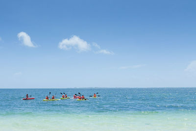 People kayaking in sea against cloudy sky