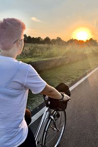 Man riding bicycle on road against sky during sunset