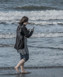 Rear view of woman using mobile phone at beach