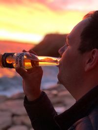 Close-up portrait of man holding ice cream against sky during sunset