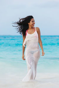 Young woman standing at beach against sky