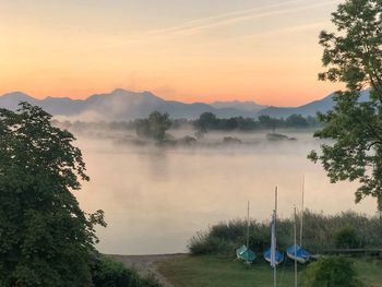 Scenic view of foggy lake against sky during sunset