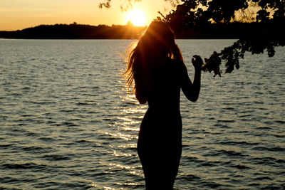 Silhouette woman standing by lake against sky during sunset