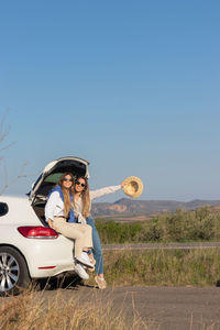 Two young pretty lady sitting in an open car boot having fun enjoying their summer road trip 
