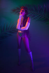 Portrait of woman smoking cigarette while standing against illuminated background