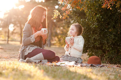 Side view of mother and daughter sitting on field