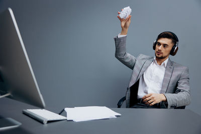 Businessman wearing wireless headphones throwing crumpled paper ball at desk
