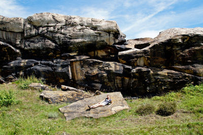 Man on rock by landscape against sky