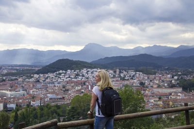 Rear view of woman standing by railing against cloudy sky