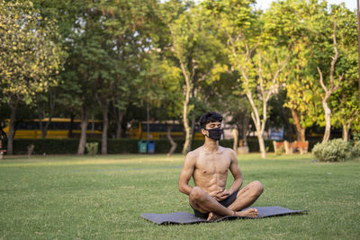 Shirtless man sitting on grass against trees