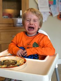 Boy crying while having food on high chair at home