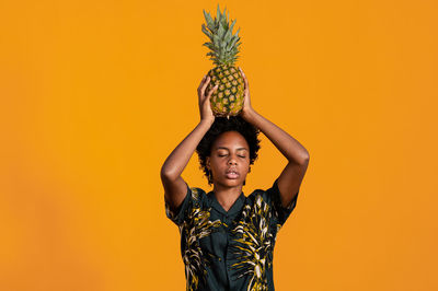 Young african american woman with short hair dressed in a summer shirt posing with pineapple