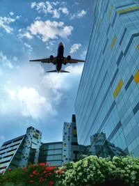 Low angle view of modern buildings against airplane flying in cloudy sky