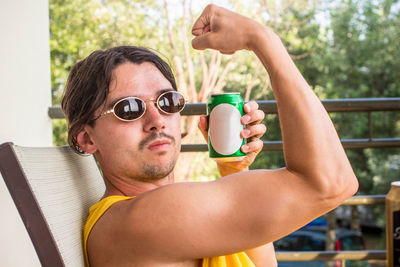 Close-up portrait of man having drink while flexing muscles on chair