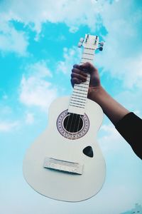 Low angle view of person holding guitar against sky