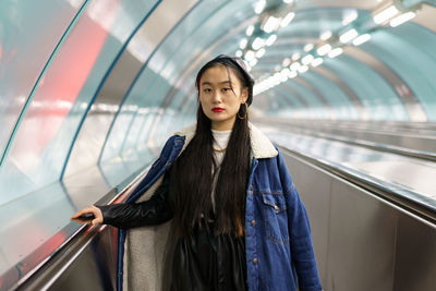 Stylish chinese girl in trendy street fashion outfit, jeans coat, leather beret on subway escalator