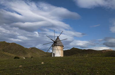 Spanish traditional windmill on field against cloudy sky. cabo de gata nature park, almeria, spain