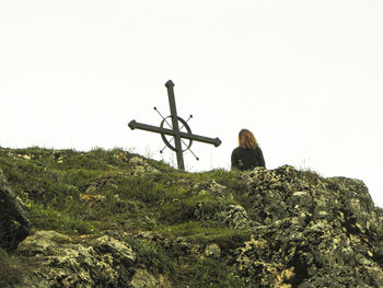 Rear view of man sitting on rock against sky