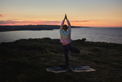 Rear view of woman standing at beach against sky during sunset