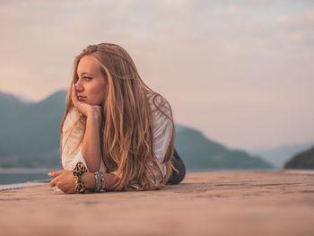 Young woman with arms raised against sky during sunset