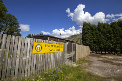 Information sign by trees against sky