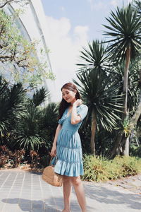 Portrait of young woman standing against palm trees