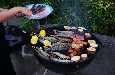 Woman putting fresh prawns on skewers on barbecue grill kitchen
