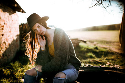 Young woman wearing hat while sitting on land