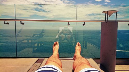 Low section of man relaxing on balcony against sea during sunny day
