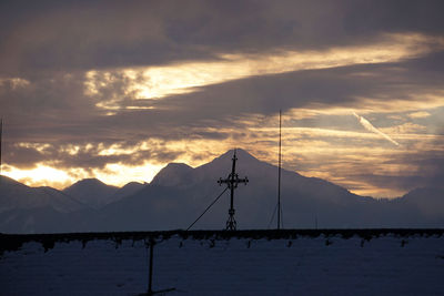 Silhouette electricity pylon by mountains against sky during sunset