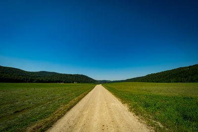 Empty road leading towards mountain against blue sky