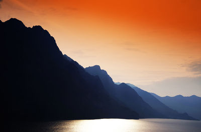 Silhouette mountain by sea against sky during sunset