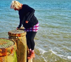 Full length of woman standing by wooden post at beach