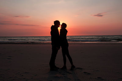 Silhouette couple standing at beach against sky during sunset