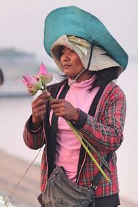 Woman holding lotus flowers against sky