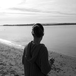 Rear view of woman standing at beach against sky