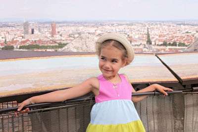 Portrait of smiling girl standing by railing against cityscape