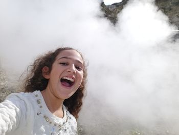 Portrait of cheerful girl standing against smoke during sunny day